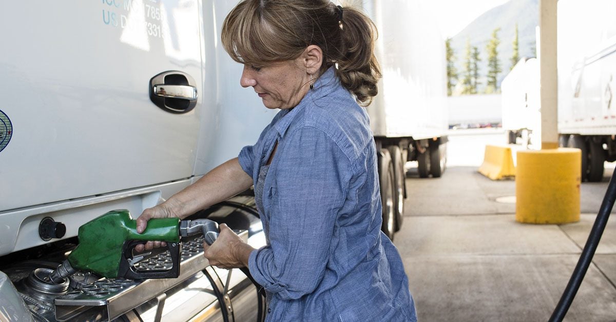 Woman fills up semi truck with diesel fuel.