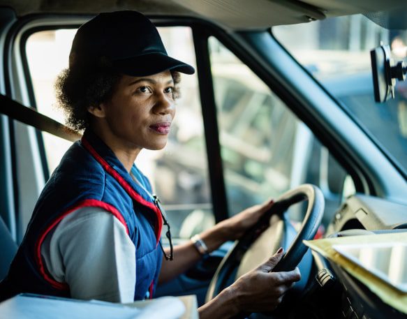 A Woman Truck Driver Sits In Her Truck Checking The Rearview Mirror Min