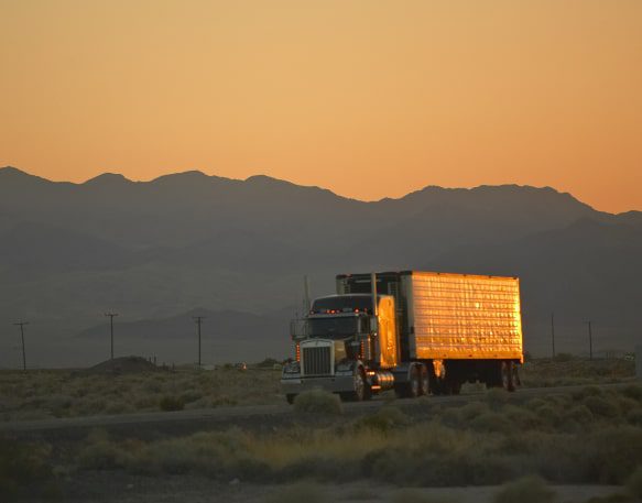 Truck Driving On The Open Road With Mountains In The Background Min