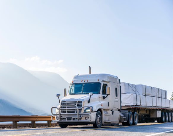 Flatbed truck driving down an open road with mountains in the background.