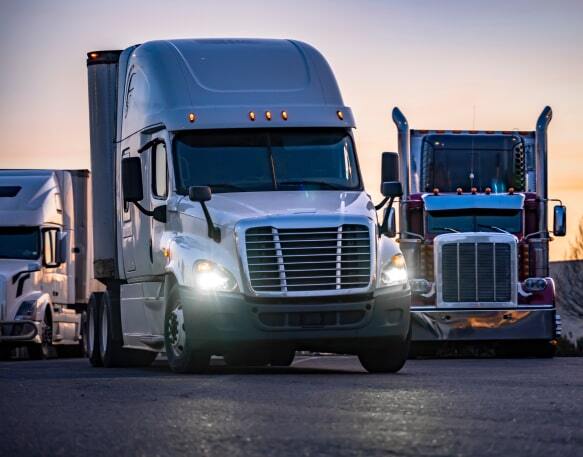 A group of big-rig semi-trucks parked in a row at a truck stop during sunset