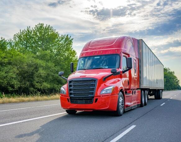 A red semi-truck driving down a highway with trees and a blue sky in the background.