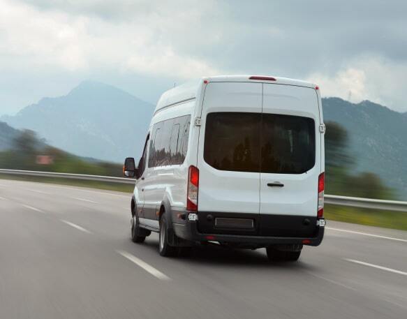 A white sprinter van accelerates on a highway with mountains on the horizon in the background.