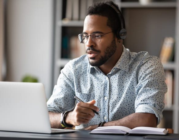 Broker sitting at his desk working and writing in notepad.