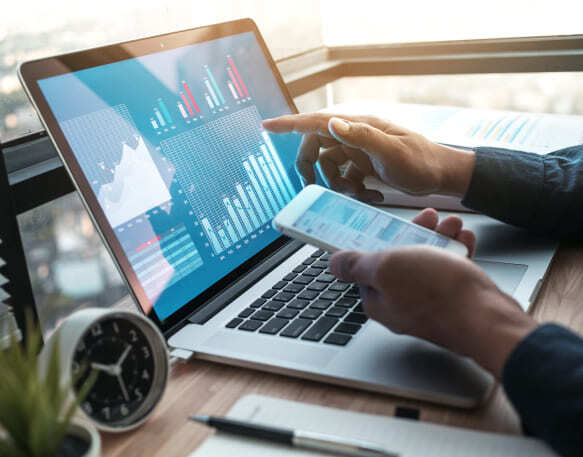 A person is using a laptop computer and a cell phone charts graphs data