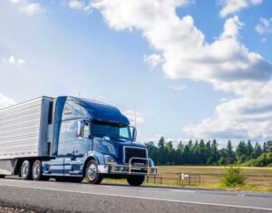 A blue commercial truck safely drives down a road on a sunny day