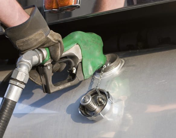A gloved hand inserts a green fuel nozzle into the fuel tank of a freight truck