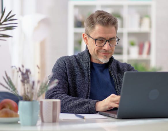 An older male professional smiling while working on a laptop in a casual atmosphere
