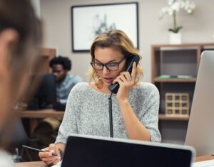 A woman is sitting at a desk talking on a phone
