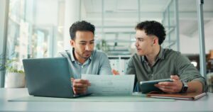 Two freight shipping professionals looking at freight data on a piece of paper discussing how to improve it