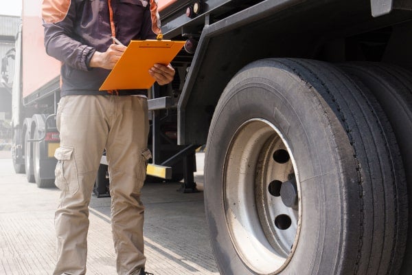A roadside inspector checks the outside of a truck.