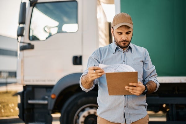 A trucker reviews information on a clipboard.