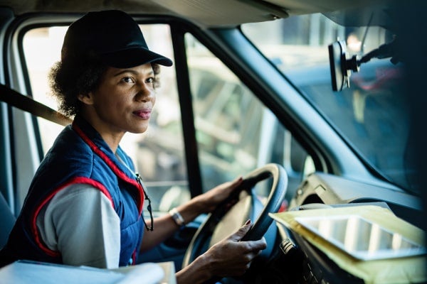 A woman truck driver sits in her truck, checking the rearview mirror.