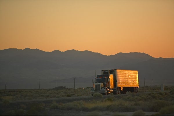 Truck driving on the open road with mountains in the background.
